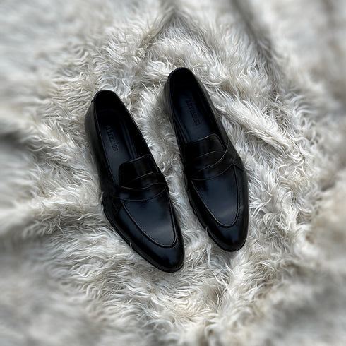 Andrew - Single component Penny loafer, made from the finest black calf leather with hand stitch detailing. The facing is adorned with a beautiful twisted leather tie, offering effortless elegance & panache