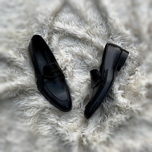 Andrew - Single component Penny loafer, made from the finest black calf leather with hand stitch detailing. The facing is adorned with a beautiful twisted leather tie, offering effortless elegance & panache